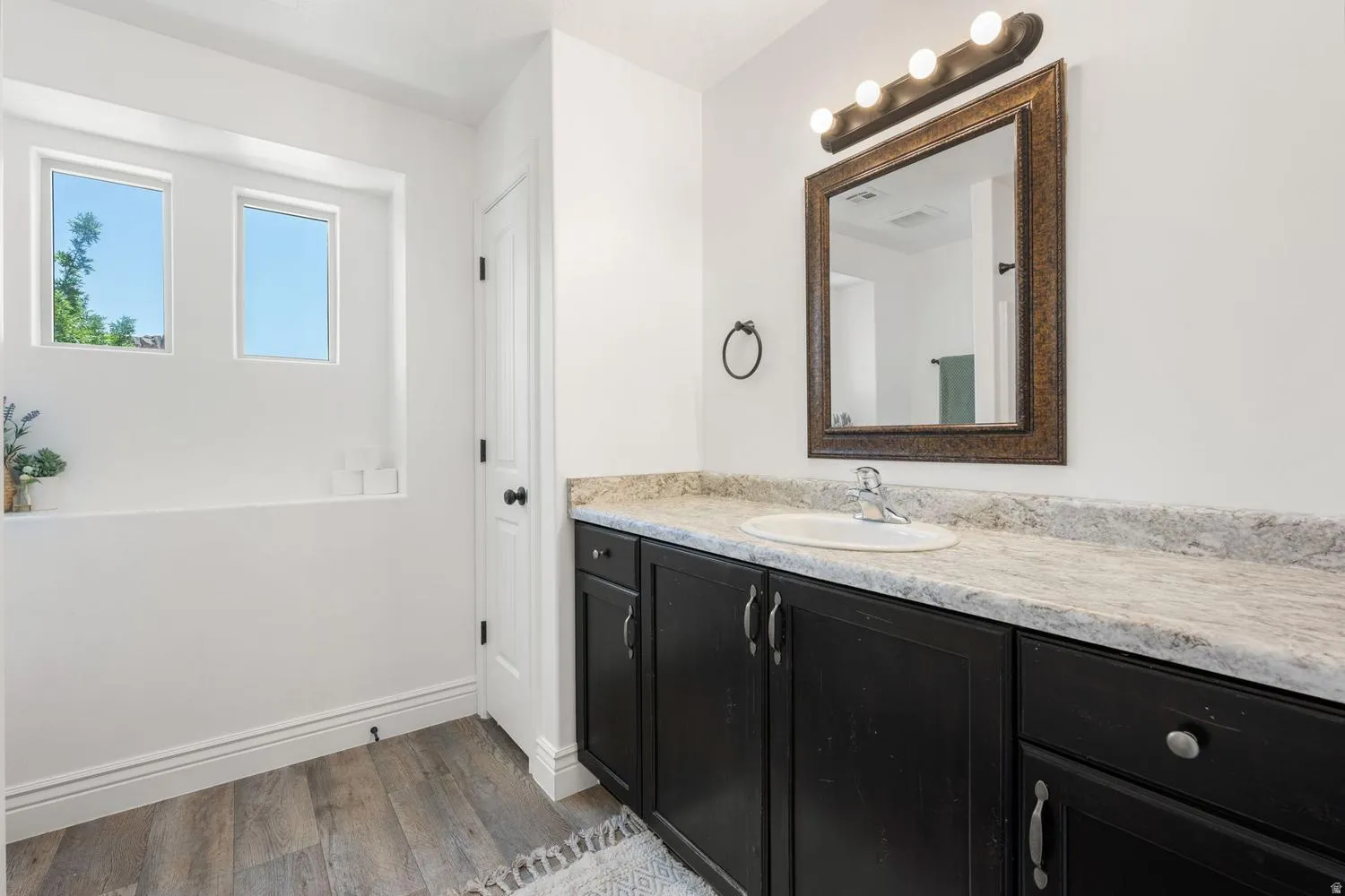 Bathroom vanity featuring a light-colored countertop, an oval undermount sink, and dark wood-finish cabinetry with silver-tone hardware
