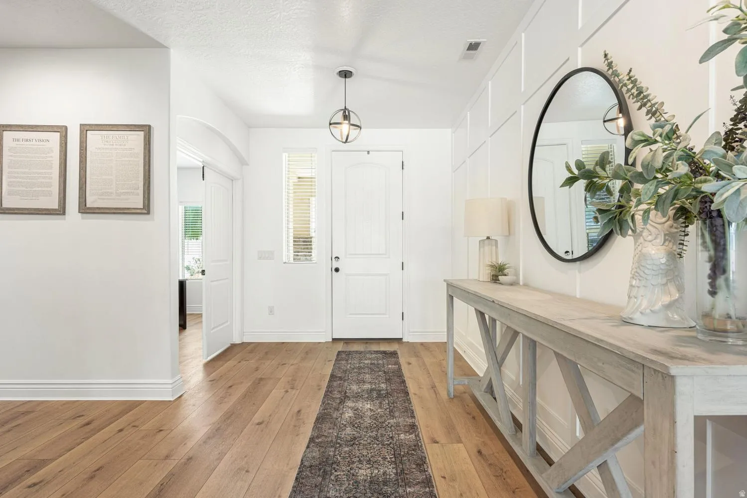 Entryway featuring wood-finish flooring, white paneling, an arched doorway, a spherical pendant light fixture, and a white front door with sidelight windows