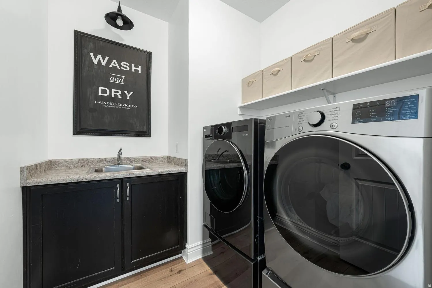 Laundry area featuring a built-in sink with a countertop, dark cabinetry, and wood-finish flooring
