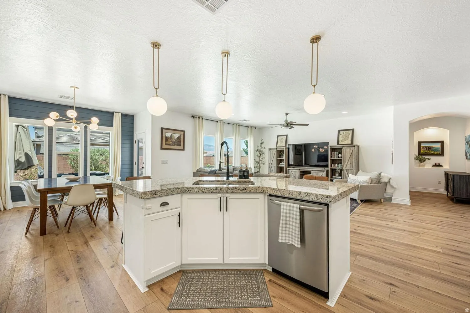 Kitchen island with stone-finish countertop, white cabinetry, integrated stainless steel dishwasher, and a black-finish faucet