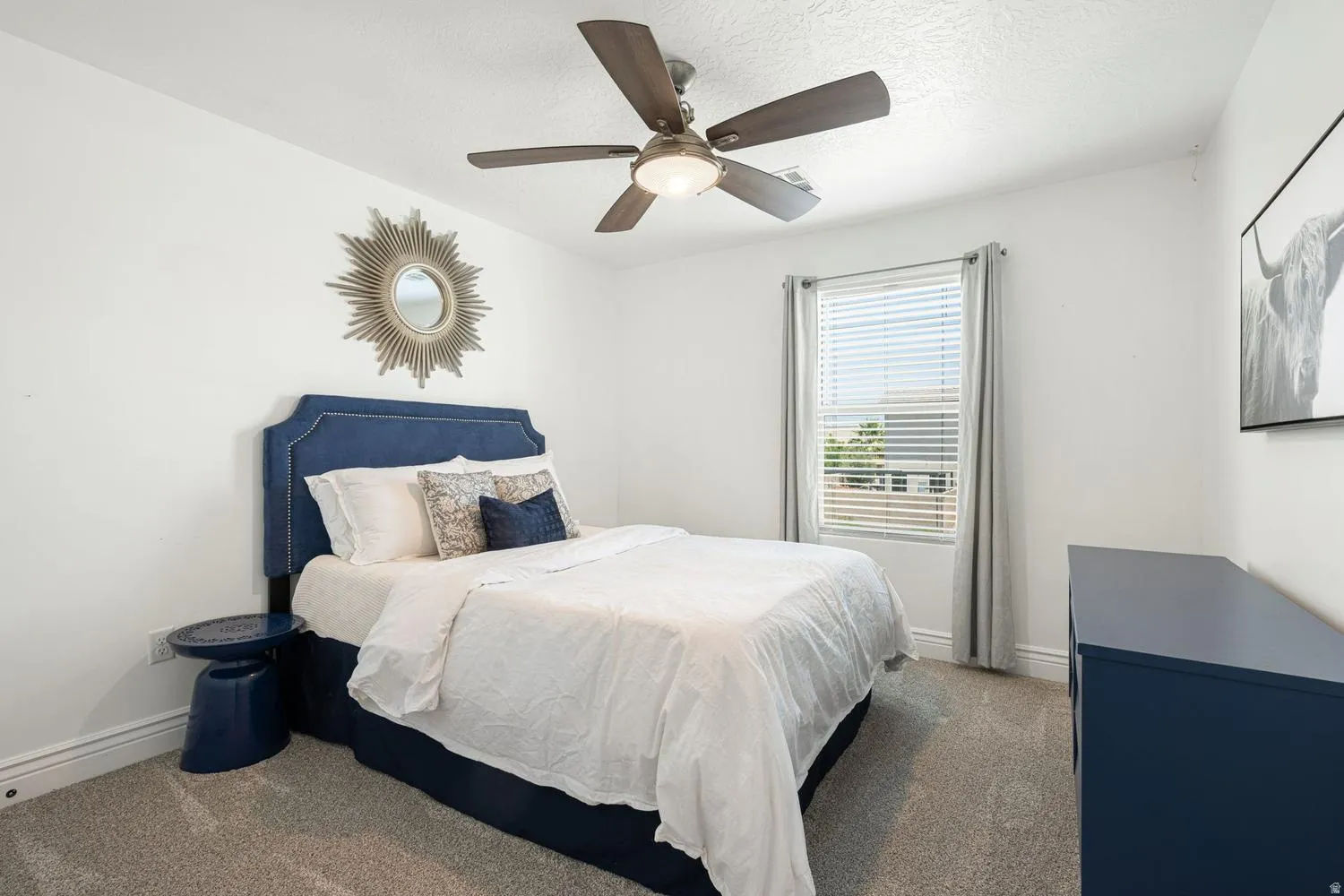 Bright room featuring neutral wall tones, plush gray carpeting, a window with blinds and drapes, and a ceiling fan with integrated lighting