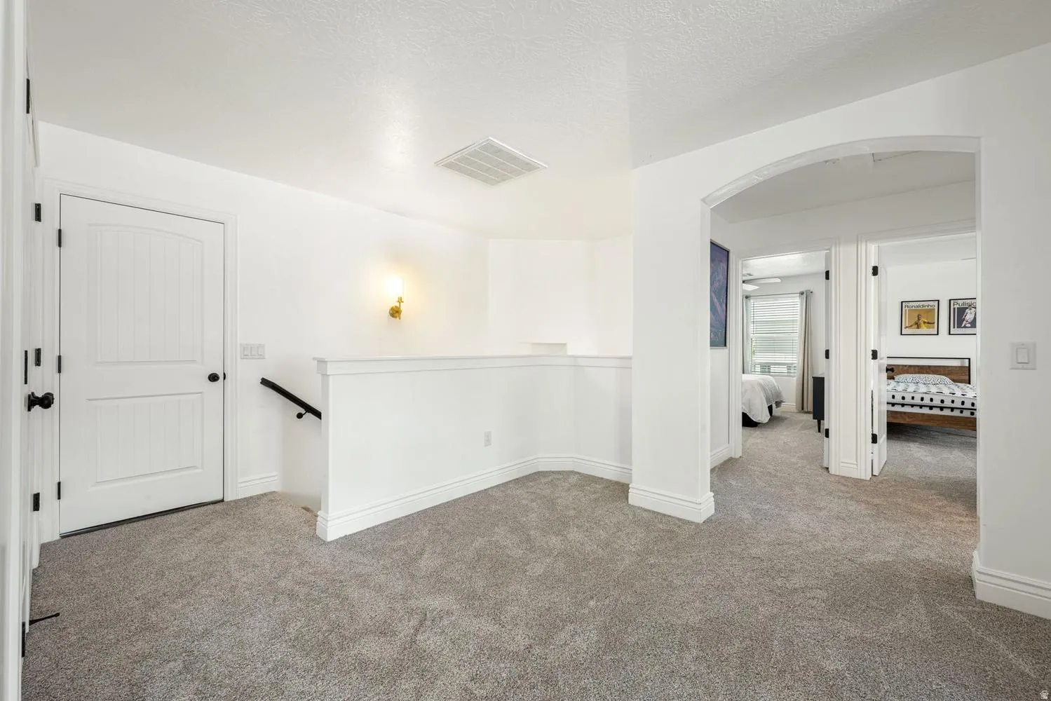 Carpeted landing with white walls and trim, featuring a wall sconce and arched entryway