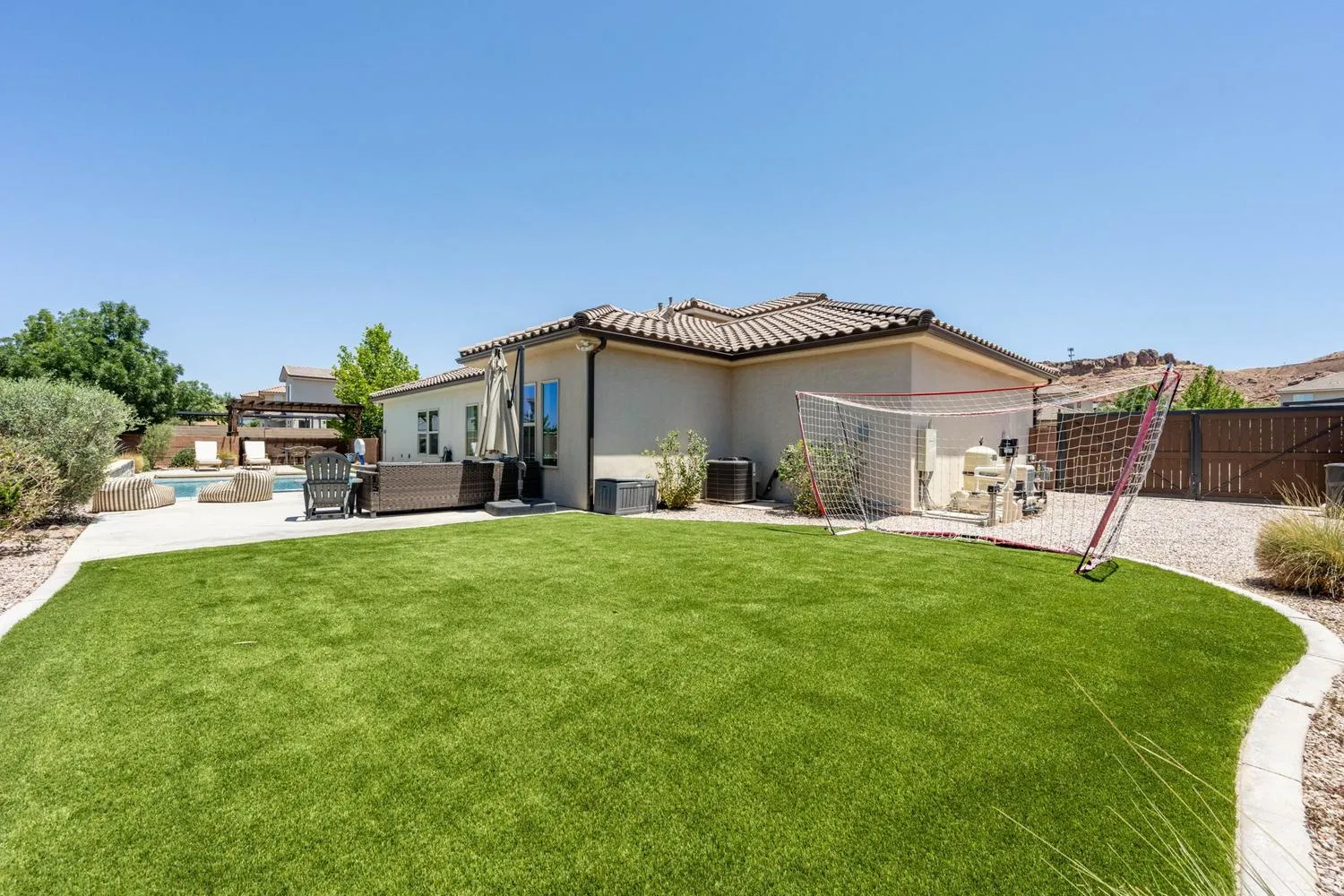Expansive backyard featuring a large artificial turf lawn, concrete patio, and in-ground swimming pool