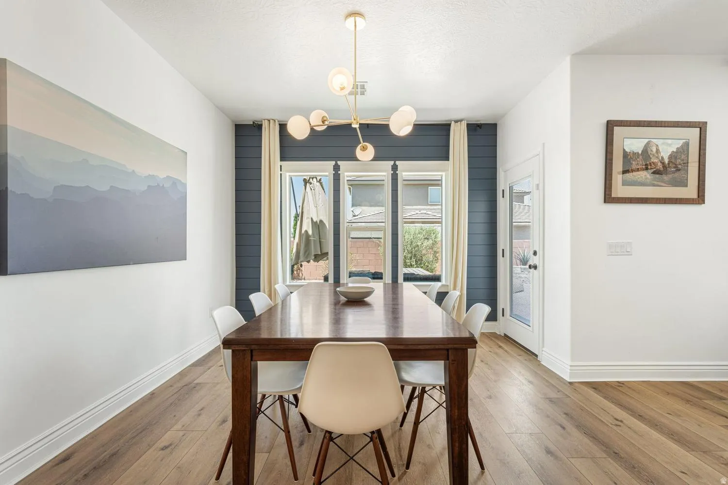 Dining area featuring wood-finish flooring, a contemporary chandelier, and a shiplap accent wall