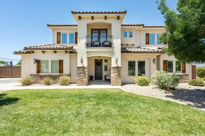 Stucco exterior with stone accents, featuring a second-story balcony with an iron railing, wood-tone shutters, a tiled roof, and an expansive lawn