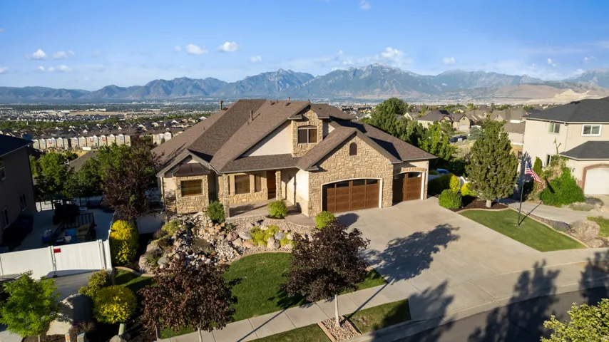 Stone and stucco exterior residence featuring a multi-gable roofline, a two-car garage with wood-finish doors, a concrete driveway, and established landscaping with valley/mountain views