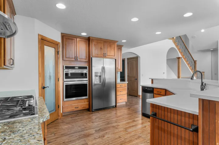 Kitchen featuring wood-finish flooring, stainless steel appliances, light wood cabinetry, granite countertops, and recessed lighting