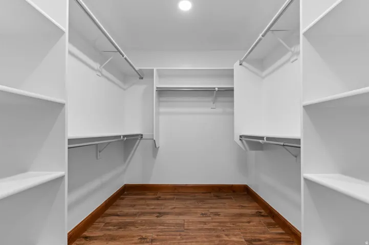 Primary walk-in closet featuring wood-finish flooring, recessed lighting, white built-in shelving, and multiple clothing rods