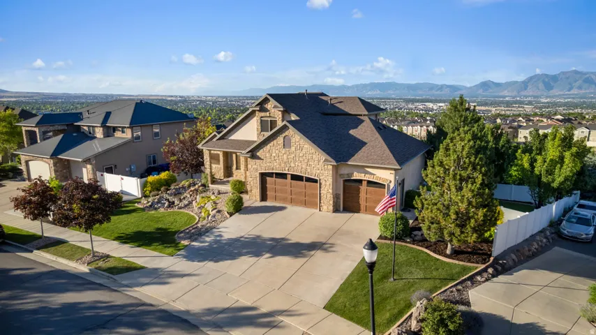 Stone-clad exterior residence featuring an attached three-car garage, concrete driveway, and established front landscaping