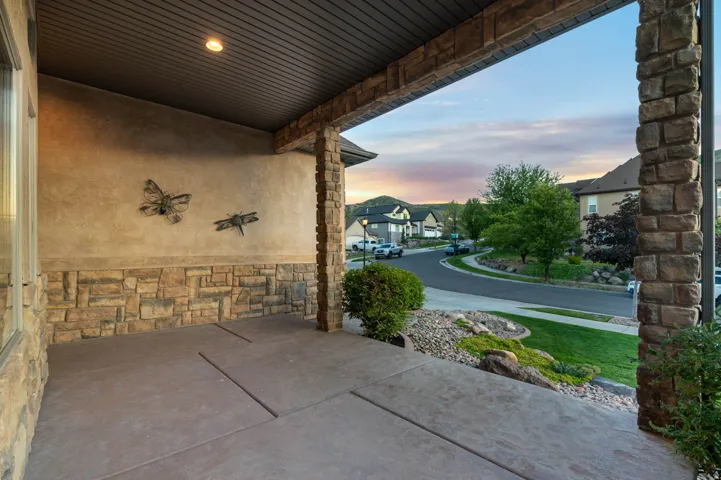 Covered front porch featuring stamped concrete flooring, stone veneer detailing, and a textured stucco wall