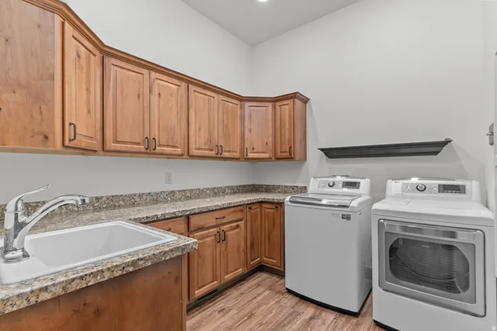 Laundry room featuring wood-finish cabinetry, speckled countertops, a utility sink with a chrome faucet, and wood-finish flooring