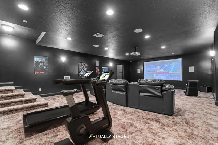 Theater room featuring a projector screen, ceiling-mounted projector, recessed lighting, wall sconces, and multi-tiered carpeted flooring
