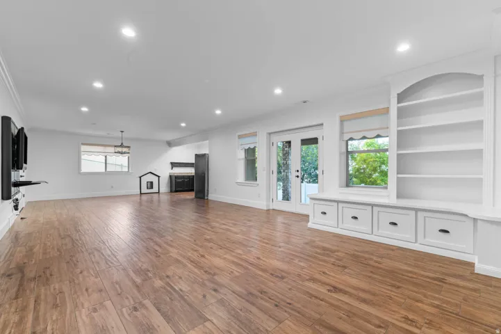 Spacious family room with wood-finish flooring, recessed lighting, and a built-in shelving unit with integrated window seating and storage drawers