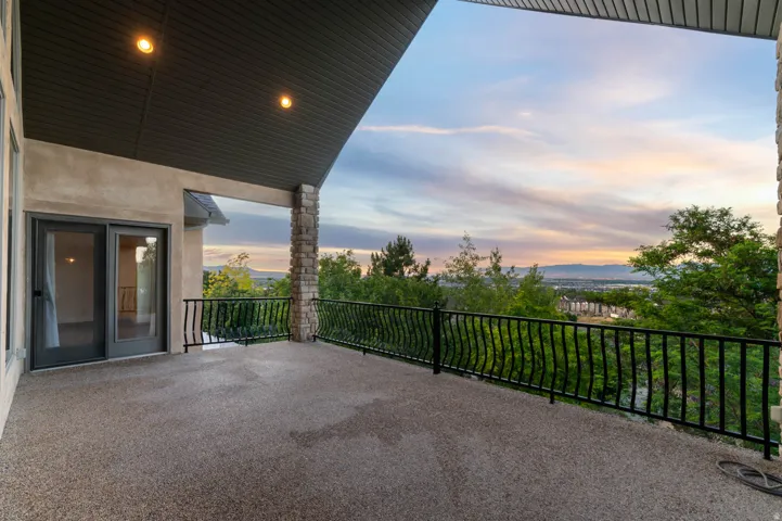 Expansive outdoor deck from main living room featuring a textured concrete surface, black wrought iron railing, and a stone pillar accent