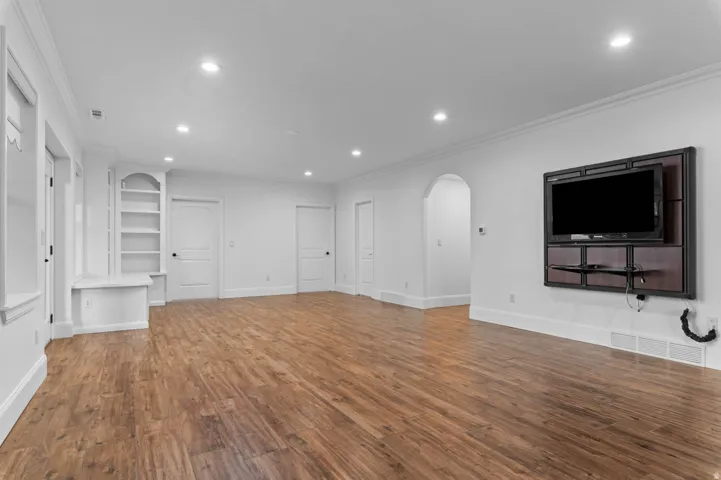 Spacious family room featuring wood-finish flooring, recessed lighting, crown molding, and built-in shelving