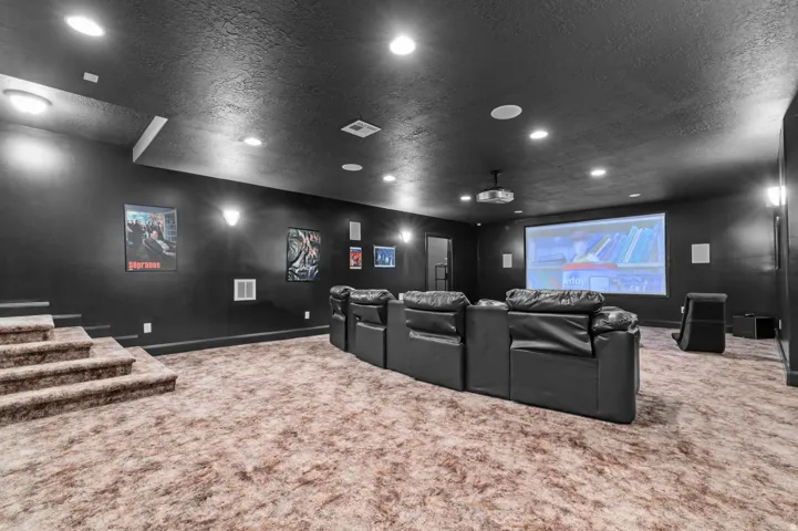 Dedicated media room featuring a projection screen, recessed ceiling lighting, wall-mounted sconce lighting, permanent sound system components, and a multi-level carpeted floor