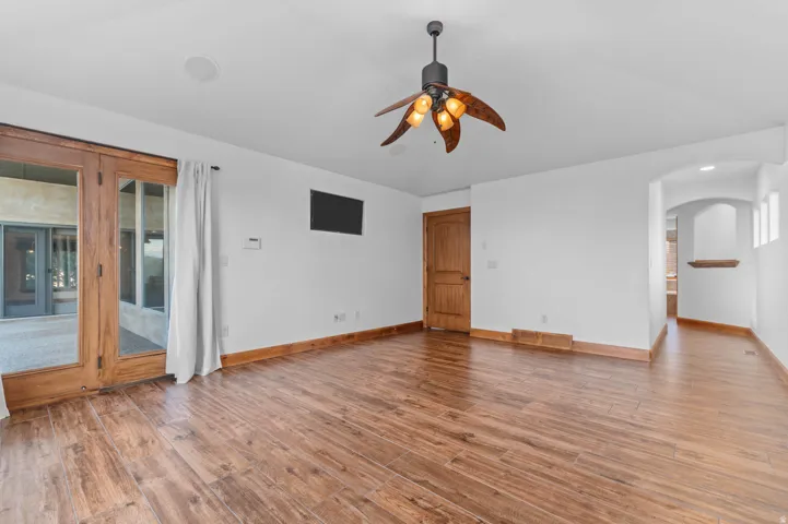 Spacious  primary bedroom with wood-finish flooring, white walls, and a decorative ceiling fan