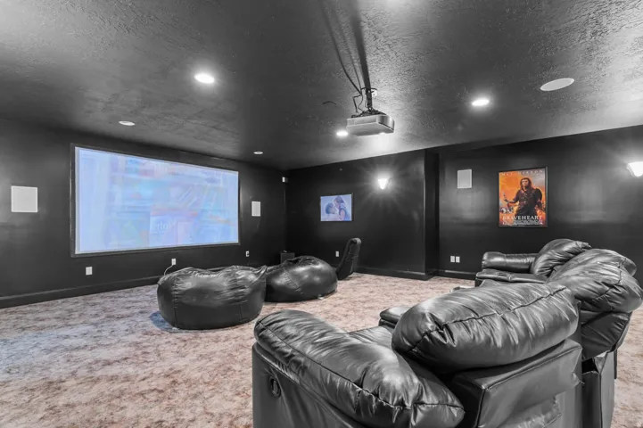 Dedicated media room featuring a large projection screen, wall-mounted speakers, recessed lighting, and wall sconces