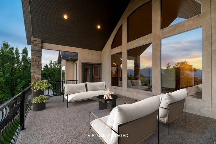 *Virtually Staged Image* Expansive covered patio featuring a textured floor, stone column accents, and a decorative metal railing
