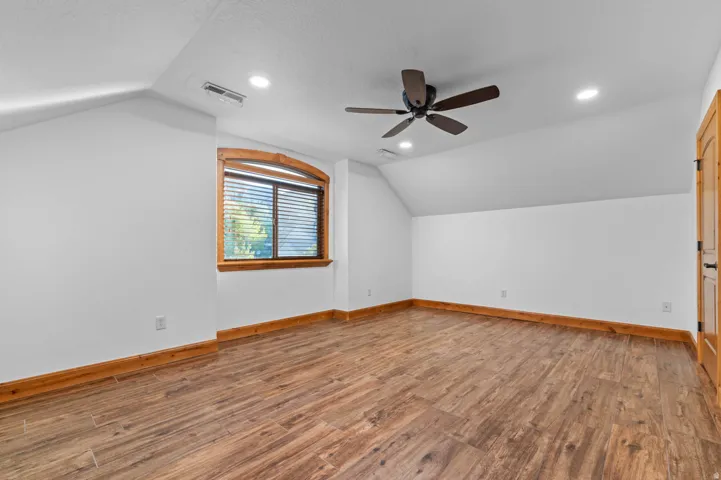 Spacious bedroom featuring wood-finish flooring, white walls, and a sloped ceiling