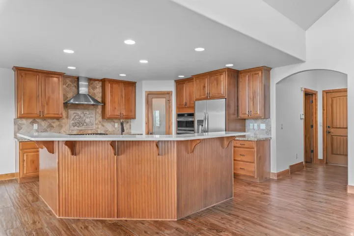 Open concept kitchen featuring an expansive central island with beadboard paneling, light-toned countertops, and rich wood-finish flooring