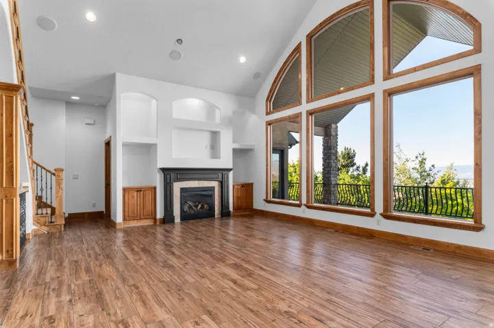 Spacious living area featuring wood-finish flooring, a contemporary fireplace with a dark mantel, built-in shelving, and large picture windows with arch details