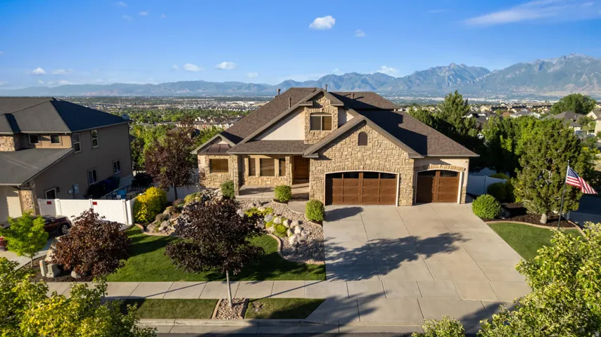 Stone and stucco exterior residence featuring a multi-car garage, concrete driveway, and established landscaping