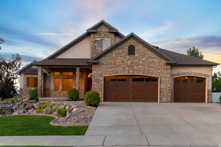 Stone and stucco exterior featuring mature landscaping with waterfall feature, a prominent multi-car garage with arched panel doors