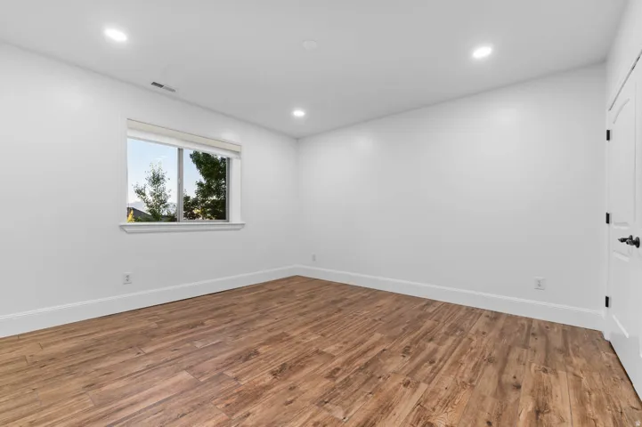 Spacious room featuring wood-finish flooring, recessed lighting, and a white interior door with black hardware