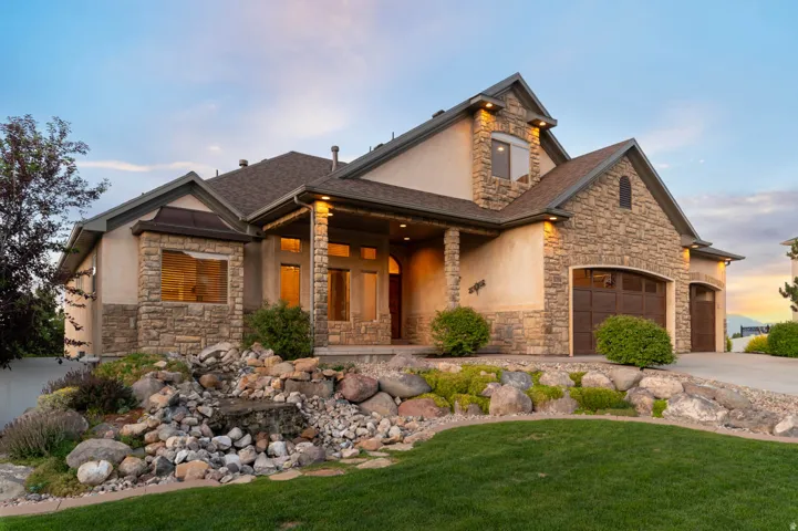 Stone and stucco exterior featuring mature landscaping with waterfall feature, a prominent multi-car garage with arched panel doors