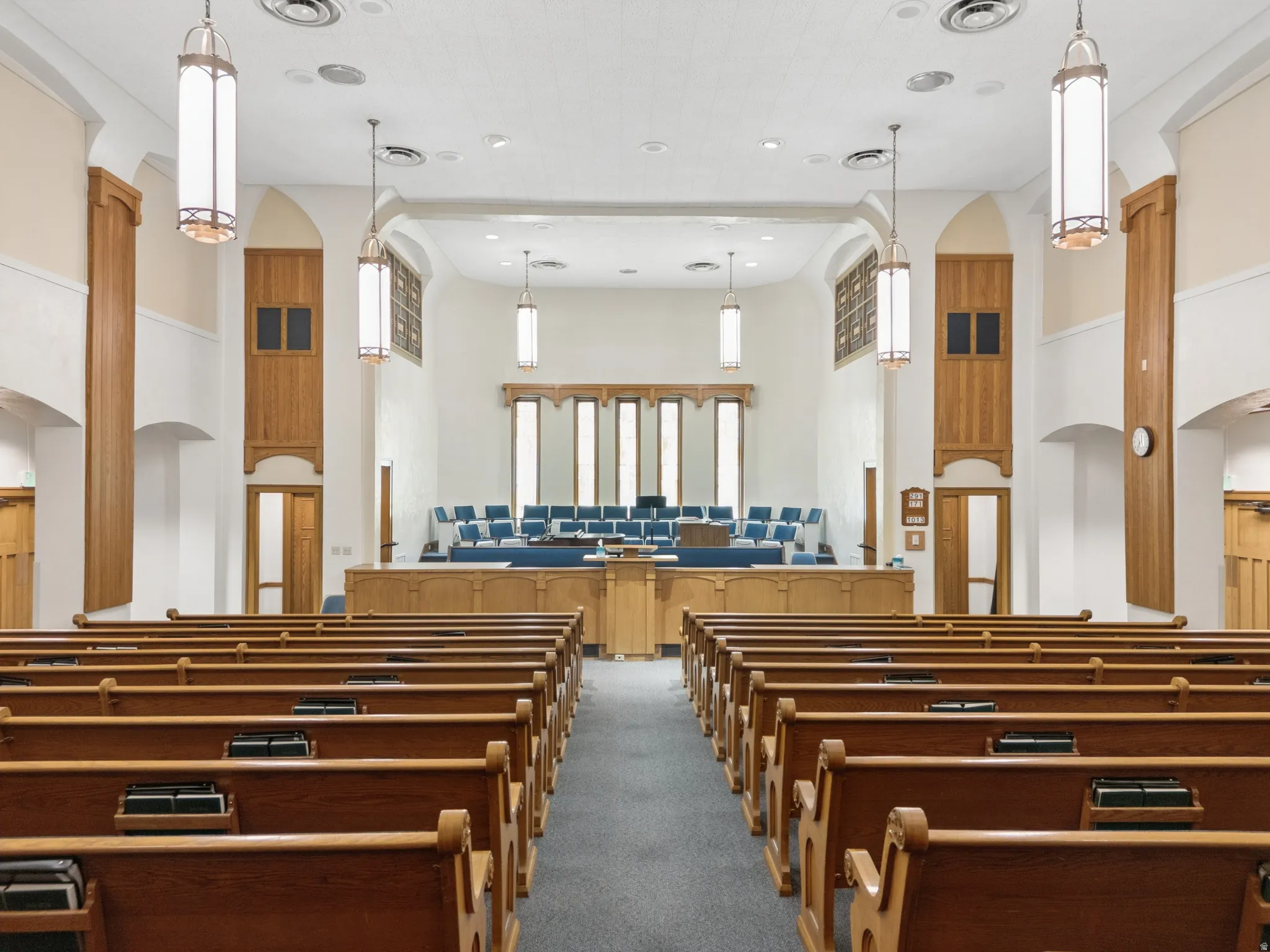 Spacious assembly hall featuring numerous wooden pews, a carpeted aisle, and a raised platform.