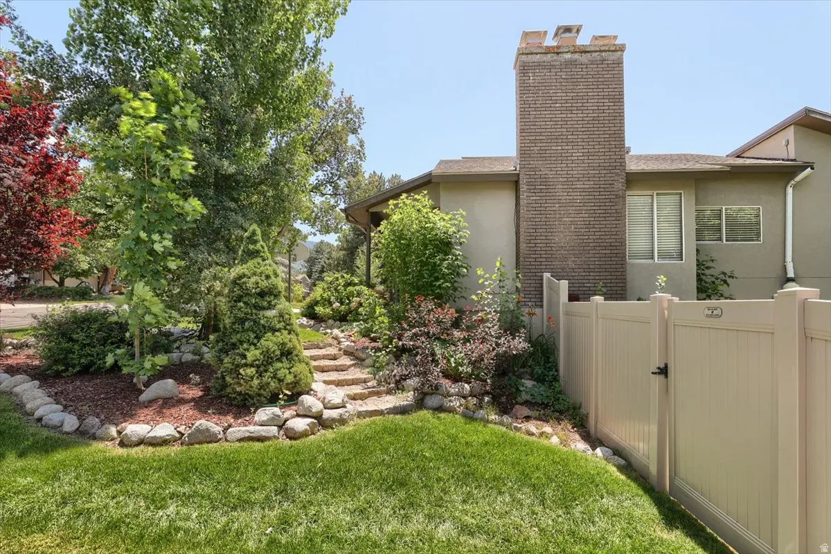Brick chimney with a stucco exterior, featuring a private fenced yard with mature trees and a stone-lined garden path