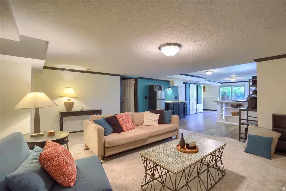 Open-concept living space featuring recessed lighting, carpet flooring, and a distinct kitchenette area with wood-finish flooring