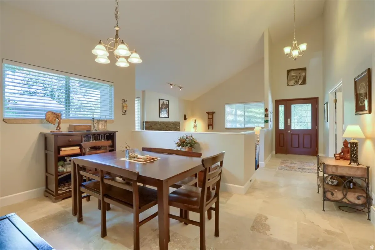 Dining area featuring vaulted ceilings, tile flooring, a large window with blinds, and a chandelier