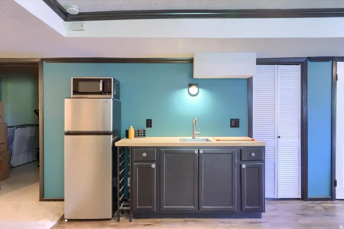 Kitchenette featuring a stainless steel refrigerator, dark gray cabinetry, natural wood-finish countertop, and a stainless steel sink with a gooseneck faucet