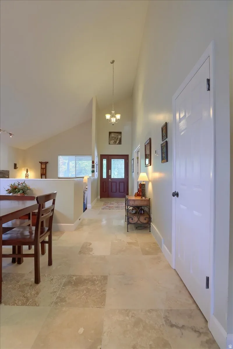 Spacious entryway featuring large format tile flooring, vaulted ceilings, a prominent chandelier, and a wood-paneled double entry door