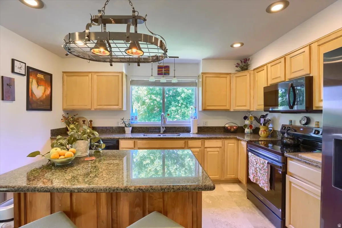 Kitchen featuring recessed lighting, a central island with a stone countertop, wood-finish cabinetry, a stainless steel sink, and a black range