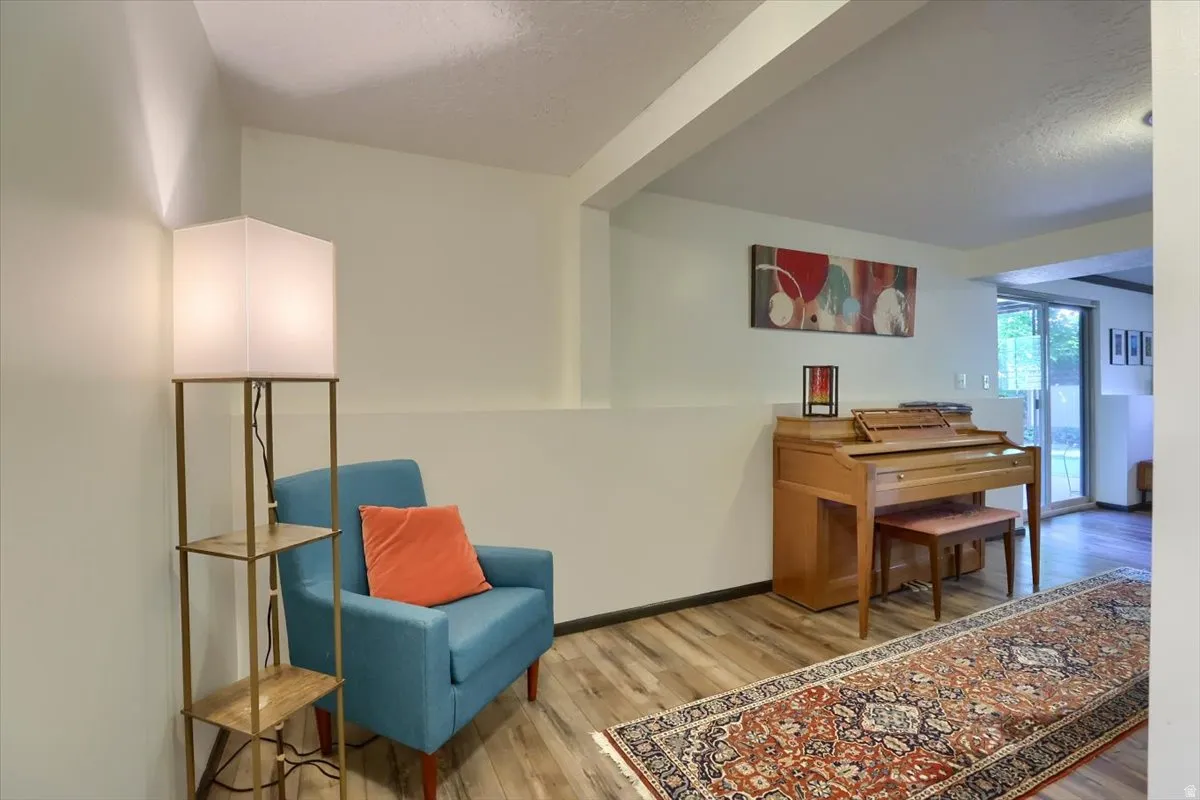 Open-concept interior featuring wood-finish flooring, white painted walls, exposed structural beam, and sliding glass door access to the exterior