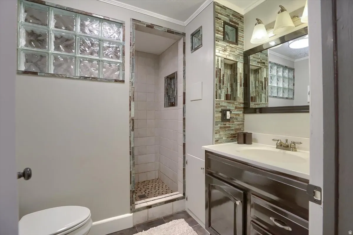 Bathroom featuring a walk-in shower with glass block window, mosaic tile accents, a dark wood-finish vanity with a single basin sink, and a large wall-mounted mirror