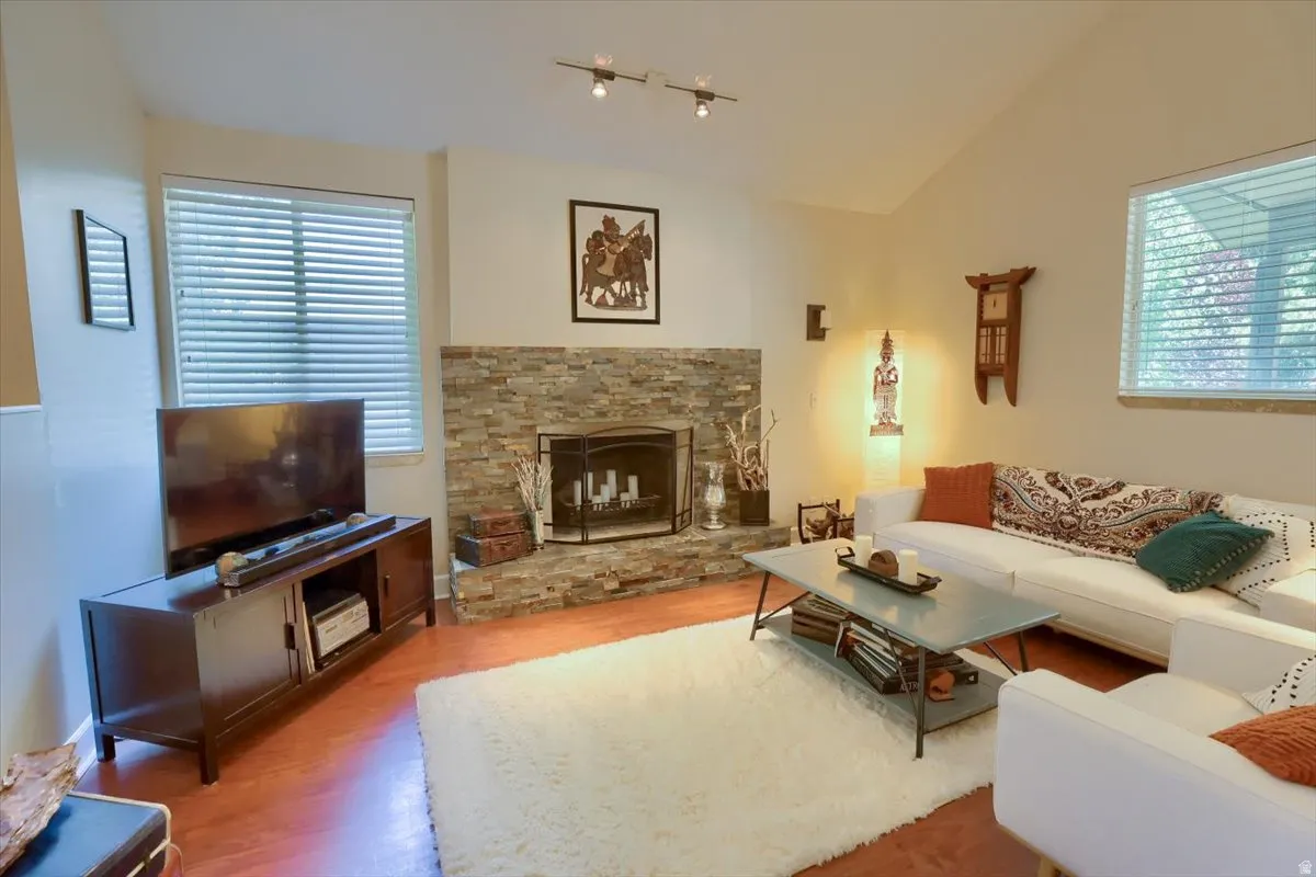 Living area featuring a stone-clad fireplace with a black metal fire screen, vaulted ceilings, and wood-finish flooring