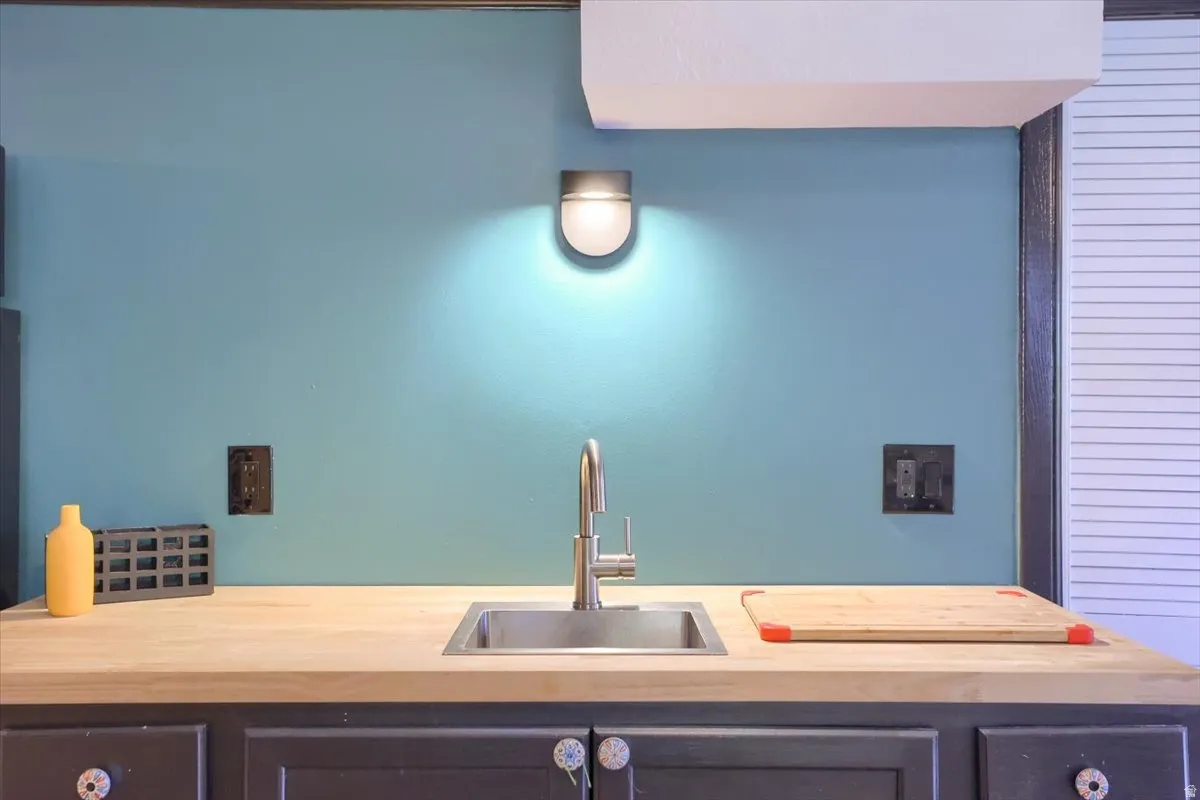 Kitchenette area featuring a stainless steel sink with a gooseneck faucet, butcher block-style countertop, and painted cabinetry with decorative knobs