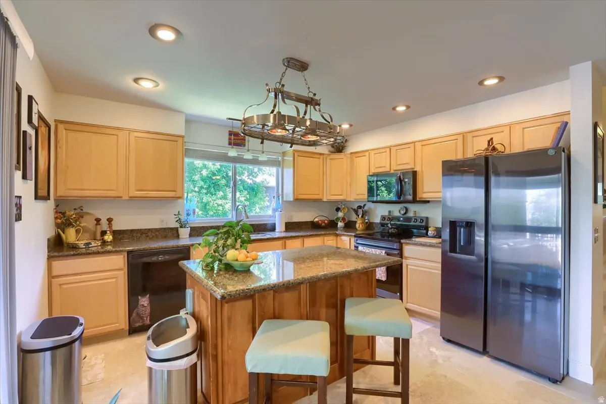 Kitchen featuring an island with a granite countertop, wood-finish cabinetry, recessed lighting, and a stainless steel refrigerator
