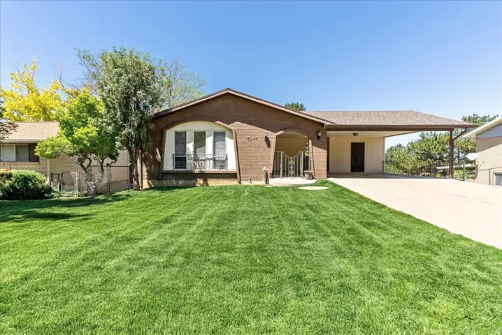 Brick exterior residence featuring a front lawn, an arched entry porch with decorative security gates, a prominent bay window, an attached carport with a shingled roof, and a concrete driveway
