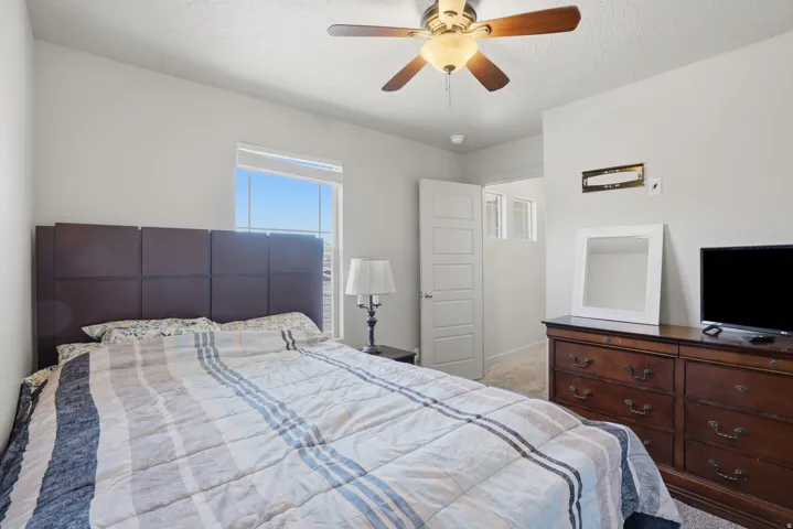 Bedroom featuring light gray walls, a window with white trim, and a ceiling fan with integrated lighting