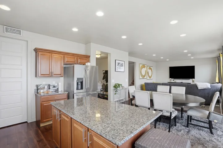 Kitchen island with granite countertop, wood-finish cabinetry, stainless steel appliances, and recessed lighting