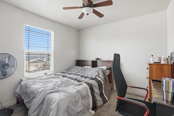Carpeted room featuring a white ceiling and walls, a window with blinds, and a ceiling fan with light fixture