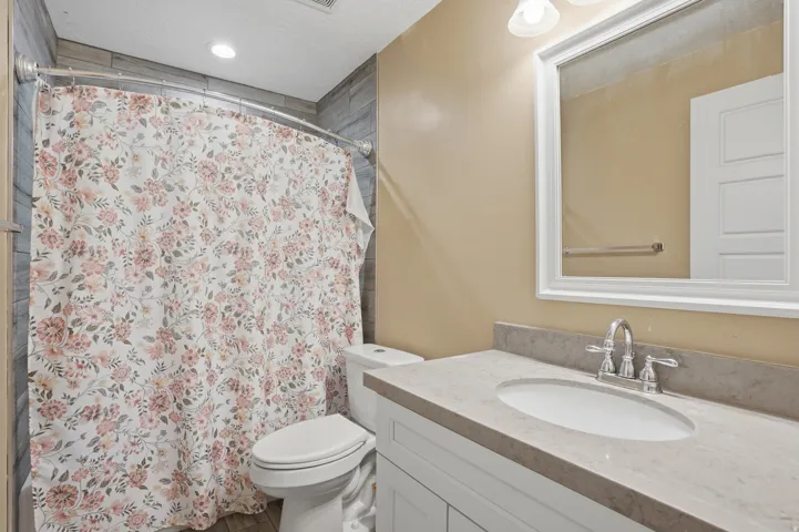 Bathroom featuring a white vanity with an oval undermount sink, a chrome two-handle faucet, and a stone-finish countertop