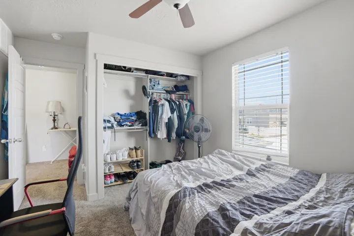 Bedroom featuring light gray walls, carpet flooring, a window with horizontal blinds, a ceiling fan, and a closet with built-in shelving and a clothing rod