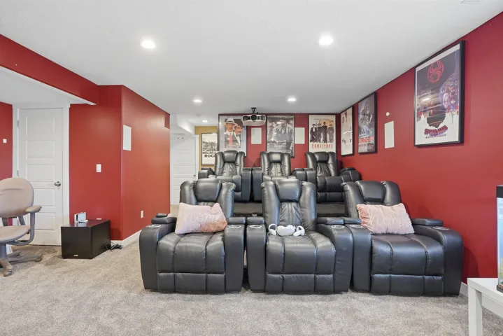 Dedicated home theater featuring tiered seating, recessed lighting, red accent walls, and gray carpeting