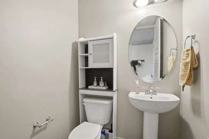 Pedestal sink with chrome faucet, complemented by an oval mirror and overhead vanity lighting